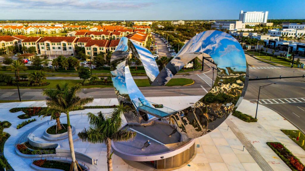 An aerial view of the large heart-shaped polished chrome sculpture in Port St. Lucie, reflecting the sky and surrounding town, representing the community served by Port St. Lucie personal injury attorneys.