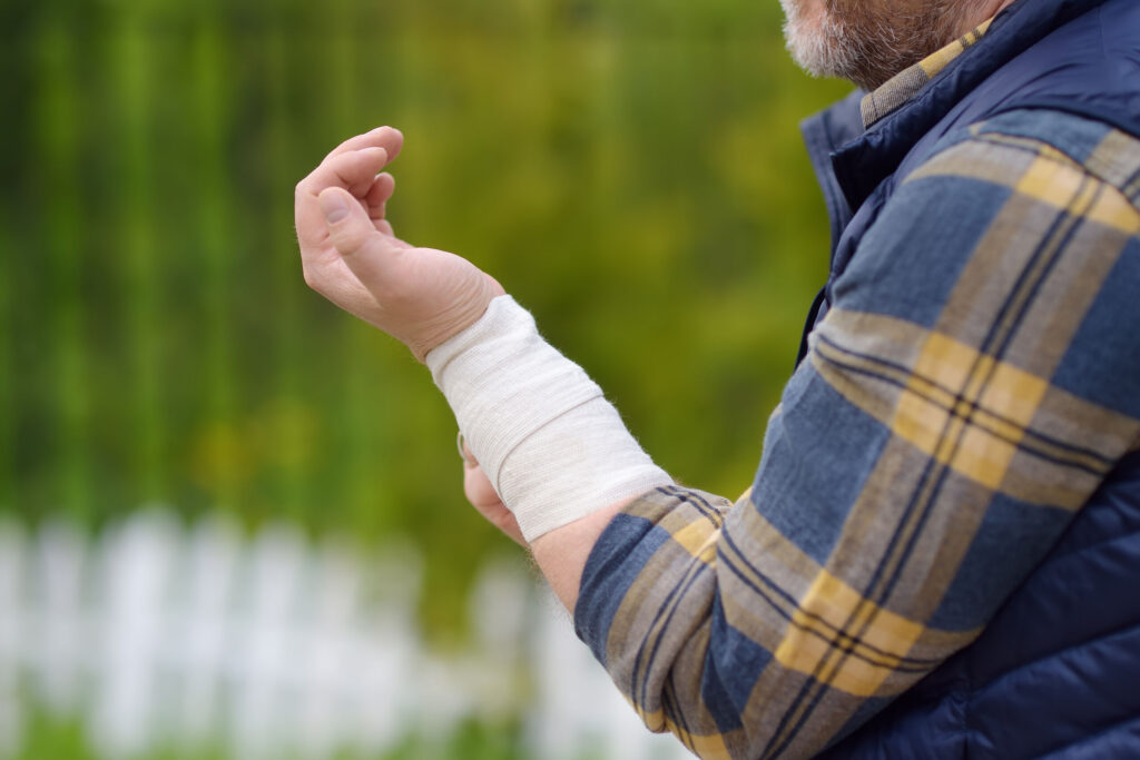 Close-up profile of a man in a plaid shirt holding up his left wrist, which is securely wrapped in a white medical compression bandage, illustrating an accident injury handled by Port St. Lucie personal injury attorneys.
